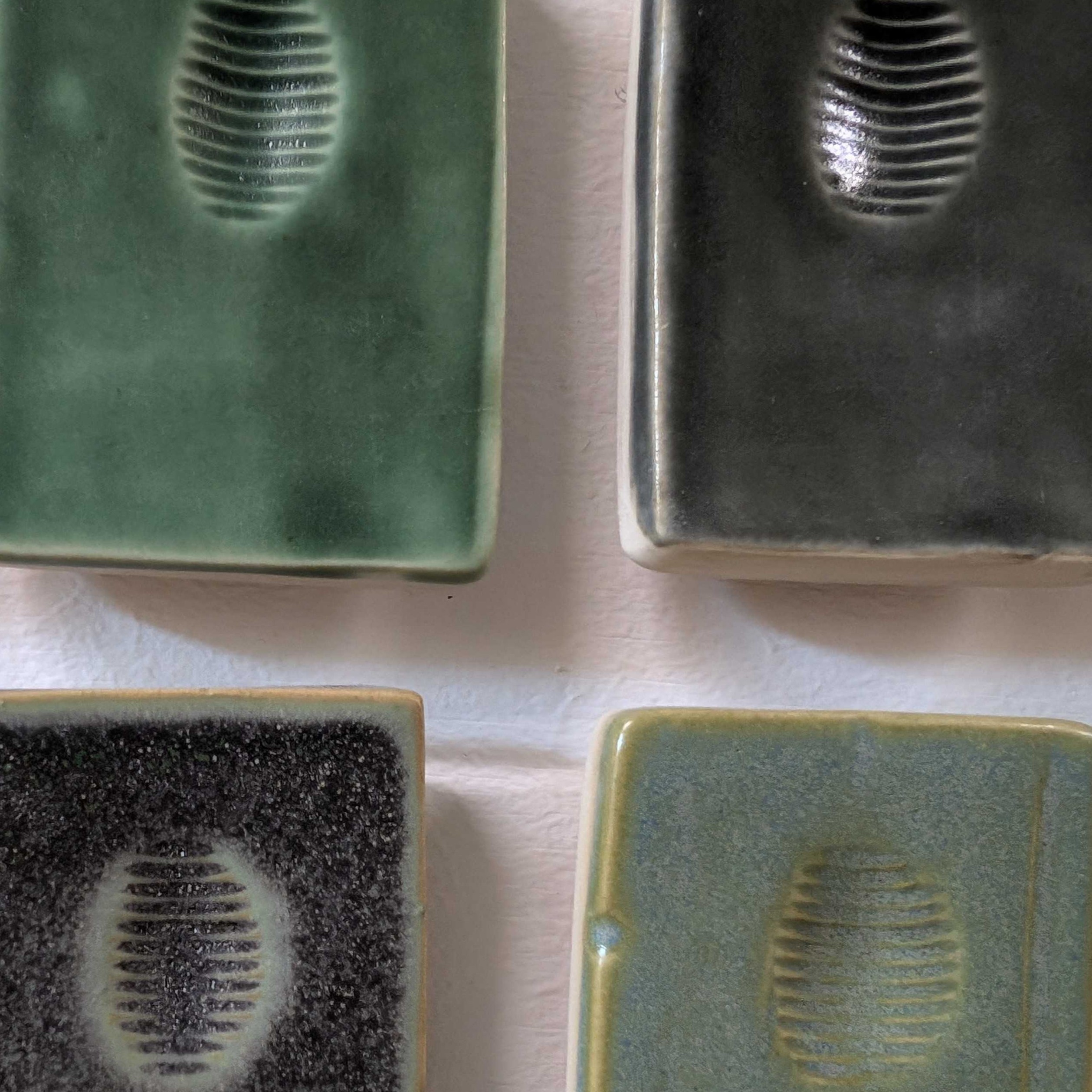 Material: Ceramic<br><br>
     These are ceramic sample tiles found in the ceramics lab hallway. They each have different
     glazes and bear ridges to show texture on how soft or harshly they appear on the glaze.
     It is a multi-day process to create ceramic from scratch. Part of its initial process
     involves sifting. A sieve is used to sift through any unwanted powder or particles from
     dry or liquid slurry. It takes time to process ceramic material, since it has to be
     hardened over time in a stove called a kiln. It also has to be reglazed, then left to dry.
     Ceramics are then painted over to reduce cracking.